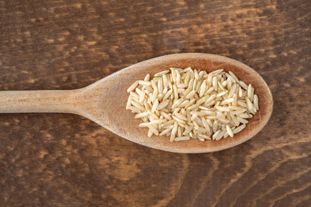 cuchara de cocina de madera con arroz integral sobre un fondo de madera oscura - brown rice fotos fotografías e imágenes de stock