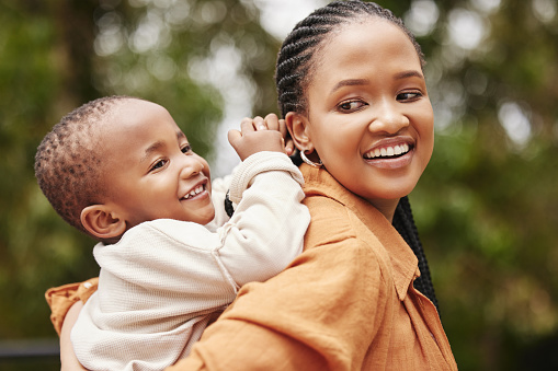 Happy mother bonding with cute baby boy on piggyback while smiling, laughing and having fun play in a park outdoors. Cheerful, loving and caring mom relaxing with playful, cute and adorable child