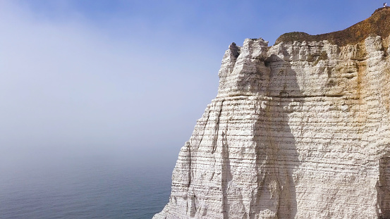 Aerial view of a beautiful white cliff on cloudy blue sky background, travel attraction. Giant steep rock above the calm sea with people walking on its top.