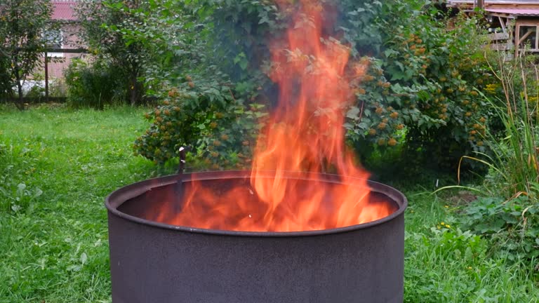 Burning garbage in yard of village house. Bonfire in metal barrel, waste disposal