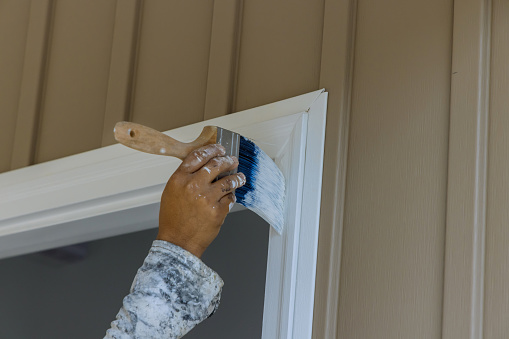 Carpenter working on painting wooden moldings door trim using the paintbrush