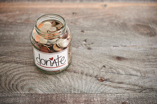 Glass jar filled with American currency for charitable donation on a wood background