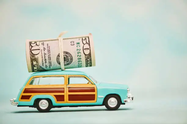 Photo of Vintage station wagon car with cash roll of American dollars on roof. Shot with copy space