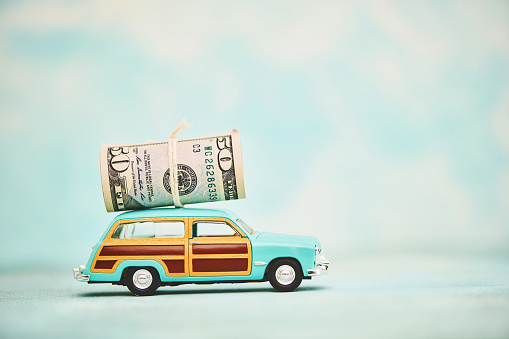 Vintage station wagon car with cash roll of American dollars on roof. Shot with copy space