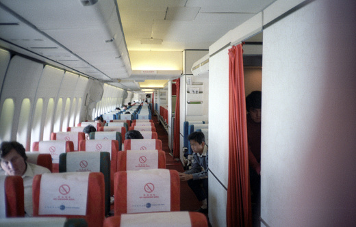 British Hong Kong, China - 1983: A vintage 1980's Fujifilm negative film scan of a China Airlines 747 airplane interior passenger cabin with red seats while the plane sits on the tarmac at the Hong Kong airport.