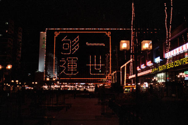 British Hong Kong, China - 1983: A vintage 1980's Fujifilm negative film scan of the downtown shopping centers of Hong Kong at night, with pedestrians, traffic, and illuminated shop signs.