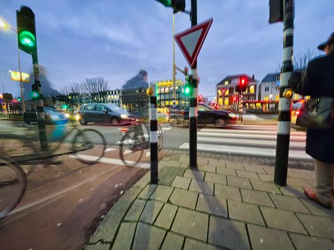 The Hague, Netherlands - December 15 2021 : a cyclist in waiting at a red traffic light before crossing the busy traffic road at night