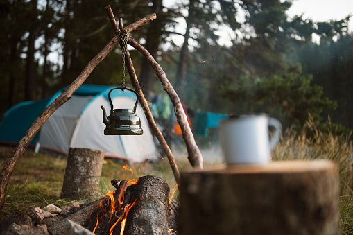 Kettle with boiling tea over open campfire on camping in the mountains.