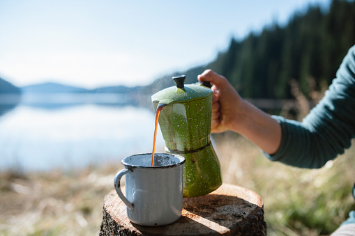 Unrecognizable woman pouring coffee from coffee pot on camping.