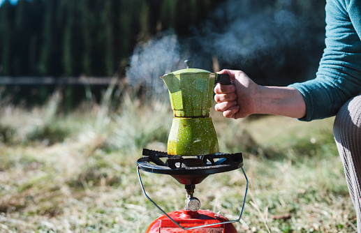 Unrecognizable woman making coffee in coffee pot on camping.