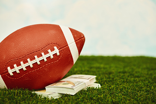 American football on turf with stacks of American dollars. Sports betting and gambling theme