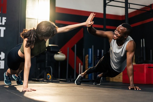 American African sportsman and Latino sportswoman work out together. Attractive athlete male and female exercising to lose weight and maintain muscle for health care lifestyle in fitness gym stadium.