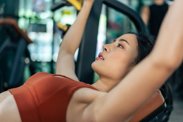 Asian sportswoman slowly lift up weight machine or barbell in stadium. Attractive young athlete female workout exercise use weight equipment tool for health care and maintain muscle in fitness club. la deportista asiática levanta lentamente la máquina de pesas o la barra en el estadio. atractiva atleta joven atleta de ejercicio femenino utiliza la herramienta de equipo de pesas para el cuidado de la salud y mantener el músculo en el gimnasio.