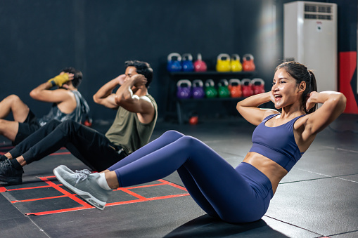 Active Sportsman and woman sit-up on floor for abs workout in stadium. Group of multiethnic fitness trainer bodybuilder people doing cardio exercise to build muscle for health care lifestyle in gym.