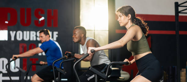 gruppo di giovani atleti che fanno esercizio insieme in palestra fitness. attraenti sportivi attivi si allenano insieme pedalando su una macchina da bici per l'assistenza sanitaria e il benessere nello stadio. - spinning health club instructor gym foto e immagini stock