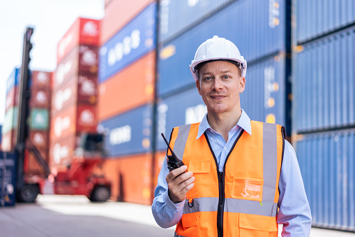 Portrait of Caucasian man worker working in container port terminal. Attractive male engineer people process orders and product at warehouse logistic in cargo freight ship for import export in harbor.
