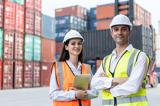 Portrait of young Caucasian business man and woman working in terminal. Attractive engineer people processes orders and product at warehouse logistic in cargo freight ship for import export in harbor.