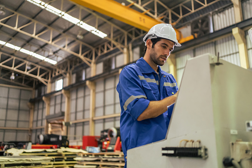 Young Caucasian male industrial worker working in manufacturing plant. Attractive handsome man industry factory engineer talk on walkie talkie with team to processes products at manufactory warehouse.