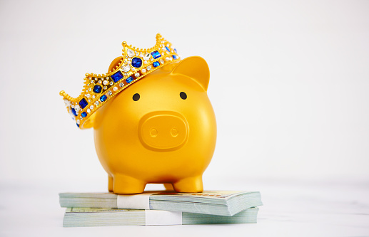 Gold piggy bank wearing crown standing on a stack of American currency