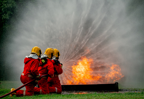 Wide shot of firefighter team with three man support together to distinguish fire using water curtain to control area of fire.