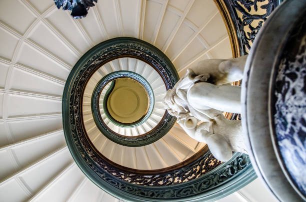 Spiral Staircase in George Peabody Library in Baltimore seen from under\n\nHans Schuler (1874-1951) was a noted Baltimore monument maker whose works include Hopkins University's Sidney Lanier and a statue of President James Buchanan in Washington, D.C. The Hopkins monument features a portrait bust of the philanthropist looking out from atop a marble pylon. On the north side of the base, a female figure holding a bowl, a serpent encircling her arm, represents healing and the hospital; on the south side, a contemplative male figure with a book and a scroll represents knowledge and the university. A fountain in front of the monument is a metaphor for the continuing impact of Hopkins' $7 million gift to Baltimore.\nBorn: Mid-19th century\n\nHeight: 55 inches\n\nMaterial: Marble\n\nAcquired: A late-1800s gift from Enoch Pratt to the Peabody Institute art gallery; the collection of 1,400-plus objects was acquired by the state of Maryland in 1996\n\nPosition: Base of the circular staircase in the Peabody Institute's lobby