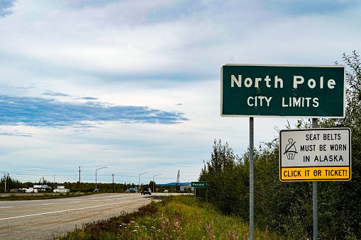 A sign marking the North Pole city limits in Alaska, USA. The mythical Santa Claus lives at the North Pole. Also, a seat belt law sign. Copy space.