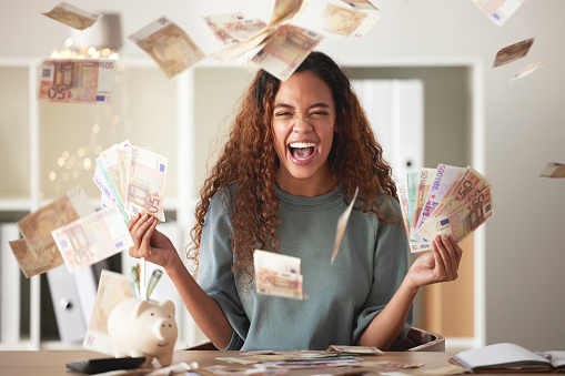 One happy young mixed race woman feeling rich and successful while throwing money at home. Excited hispanic celebrating after saving and budgeting finances. Planning for the future or win a lottery
