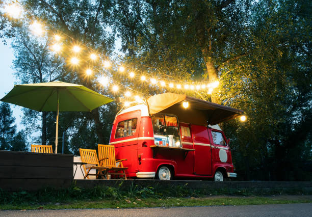 piccola pista di cibo di strada vuota con un'illuminazione in piedi nel parco notturno deserto. vicino al rimorchio del cibo ci sono tavoli e sedie pieghevoli - food truck foto e immagini stock