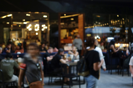 Blurred abstract background of outdoor cafe or restaurant. Outdoor cafe with tables and chairs. Street cafe in the evening in modern terrace. Customers sit at tables in a terrace area outside cafe