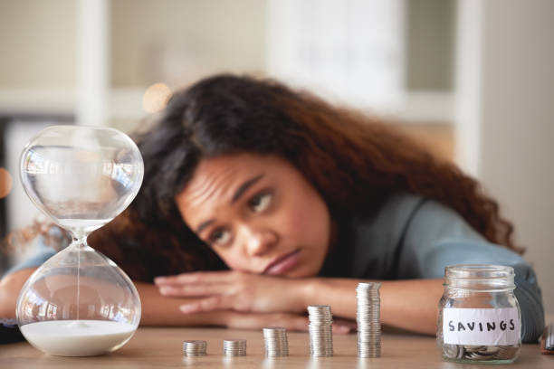 young african american woman staring at an hour glass while looking bored at home. mixed race person counting down while financial planning in her living room. waiting for her investments and savings - waiting women clock boredom imagens e fotografias de stock