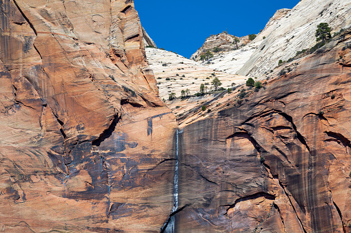 Close up of the steep mountains walls inside the canyons of the Zion National Park in Utah, United States. In the middle a waterfall.