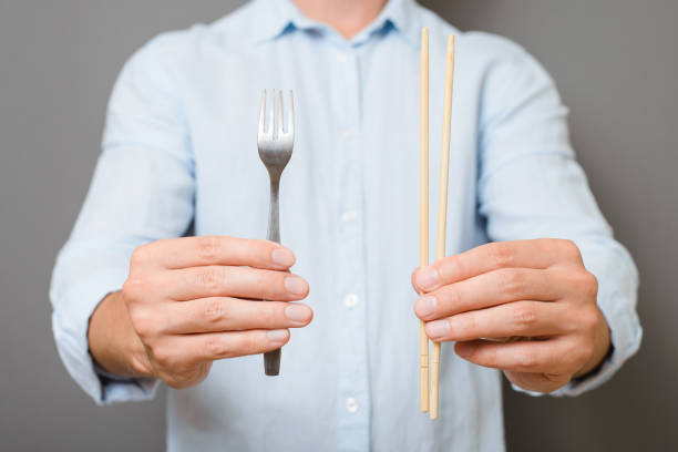 istock Unrecognizable man showing fork and chopsticks of asian traditional cuisine while standing against gray background indoors, closeup 1420053318