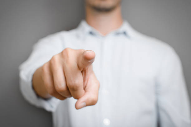 Close-up of an unrecognizable man in a blue shirt pointing his finger at the camera. Selective focus on fingertip stock photo