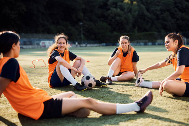 istock Soccer player and her teammates talking while relaxing on grass after sports training. 1420056991