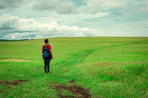 View of traveler man on a beautiful road in the countryside. Young explorer man walking in a green field, Backpacker man walking in a beautiful field.