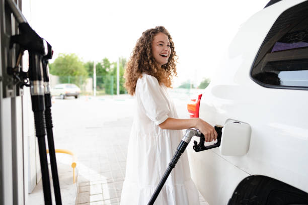 молодая кудрявая женщина заправляет машину на заправке - gasoline filling gas station car стоковые фото и изображения