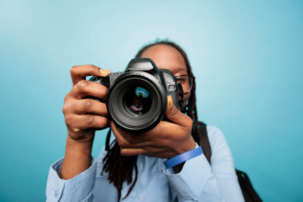 Amateur photographer taking photos with modern DSLR device while standing on blue background
