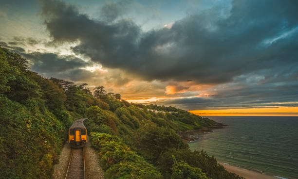 scenic view of train moving through rugged coastal area in evening at sunset; sunset sky in background - transportation railroad track train railroad car imagens e fotografias de stock