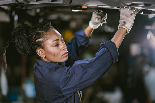 Black african woman mechanic staff worker work service under car in dirty garage