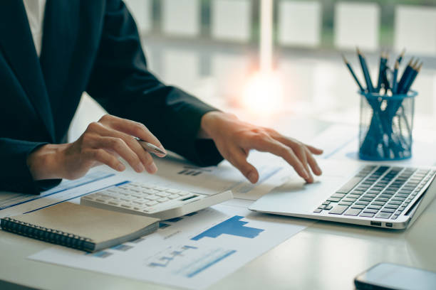 An accountant presses a calculator, calculates finances, analyzes graphs, reports finances at a desk in the office.