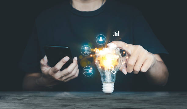 hand touching a light bulb and there is a gear icon in it and he is using a smartphone, and online shopping icons. innovation idea concept. stock photo