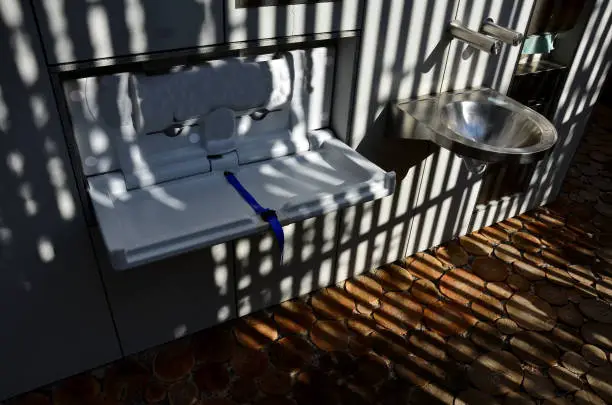 Photo of stainless steel sink with automatic battery reminds the interior of an airplane. however, it is on the bike path by the public toilets. There is also a changing table for babies, folded out