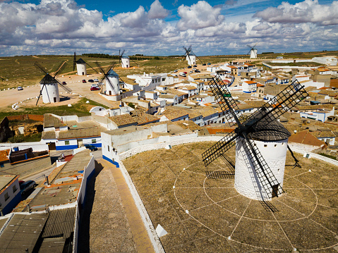 Aerial view of white cylindrical towers and pointed roofs of old Spanish windmills on background with Campo de Criptana cityscape