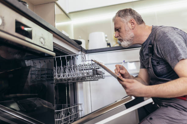 istock Male Technician Sitting Near Dishwasher Writing On Clipboard In Kitchen. 1420074026