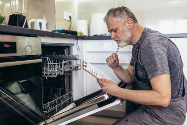 istock Male Technician Sitting Near Dishwasher Writing On Clipboard In Kitchen. 1420074030