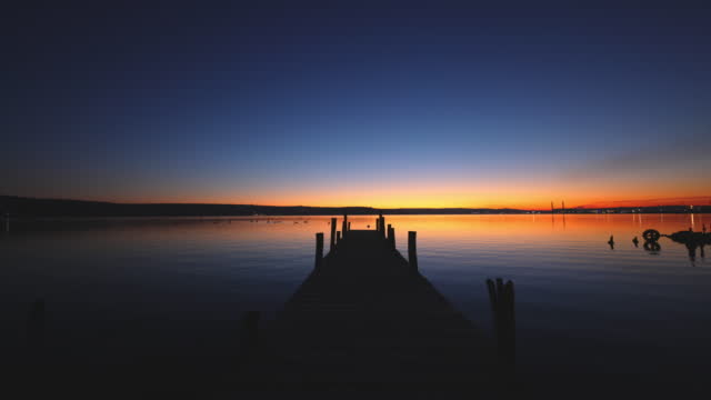 Small Dock and Boat at the lake and colorful sunset over the water. Lonely fishing jetty nature landscape.