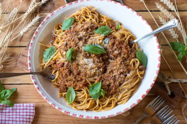 Fresh and homemade cooked traditional Spaghetti Bolognese. Served ready to eat with parmesan cheese in a large family bowl on rustic and wooden table background.