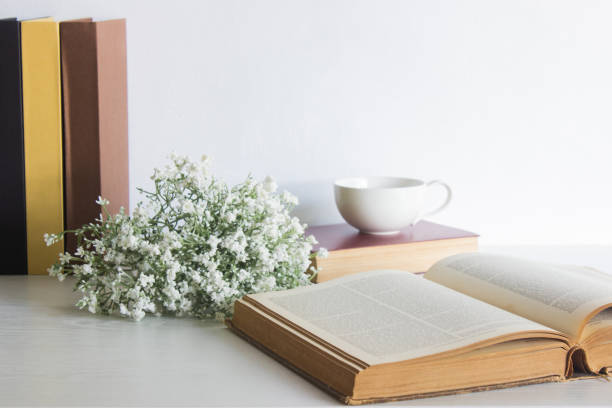 Various books with white flowers and coffee cup over the white table.