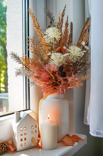 Sweet Home. Still life details in home on a wooden window. Autumn decor on a window, dried flowers, candle and toy house
