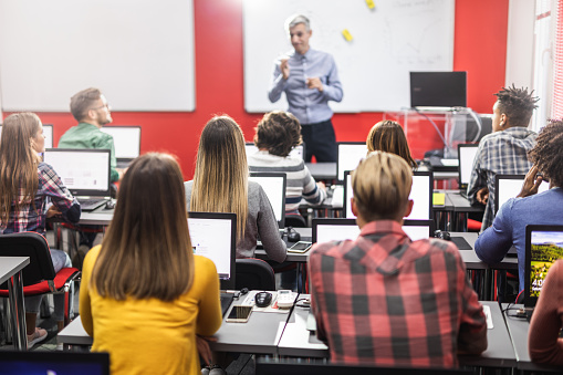 Group of adult students attending computer course. Focus on teacher talking with an adult man.